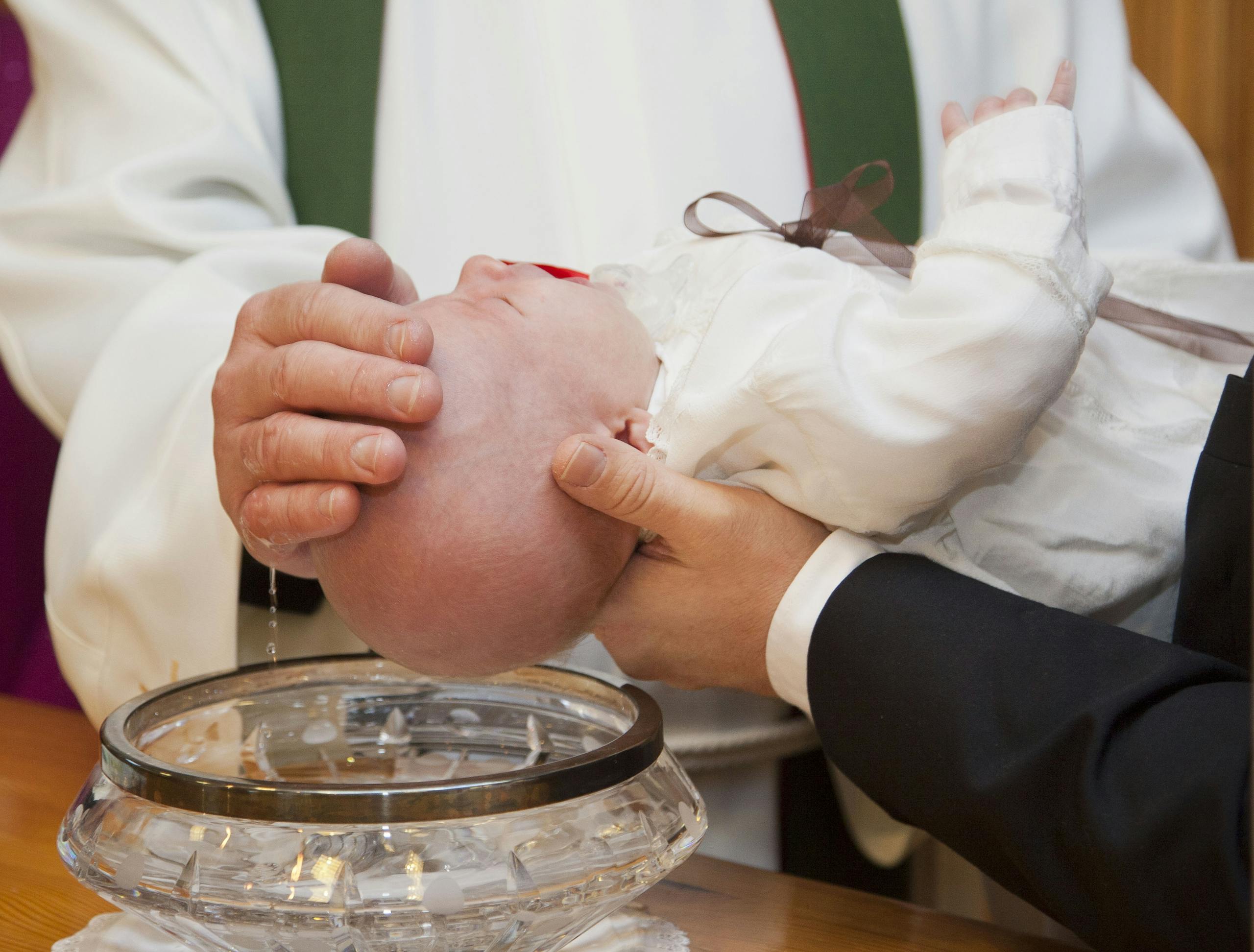 A baby being baptized during a ceremonial Christian baptism, featuring a priest and holy water.