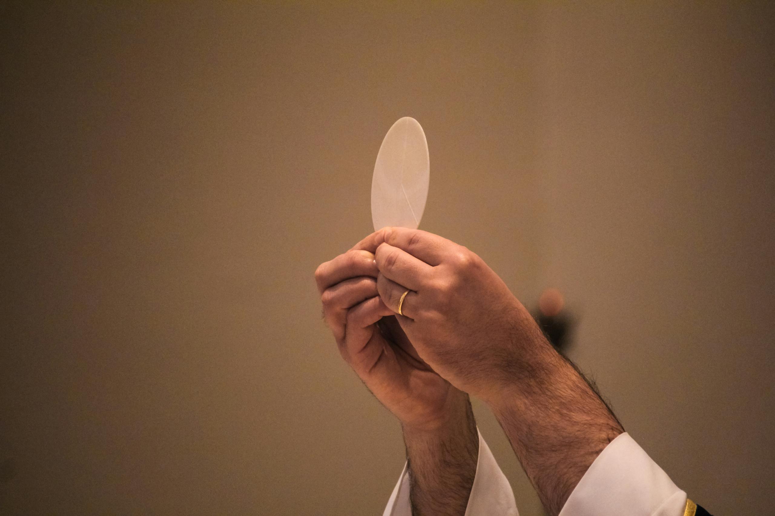 Priest's hands holding a communion host during a religious ceremony indoors.